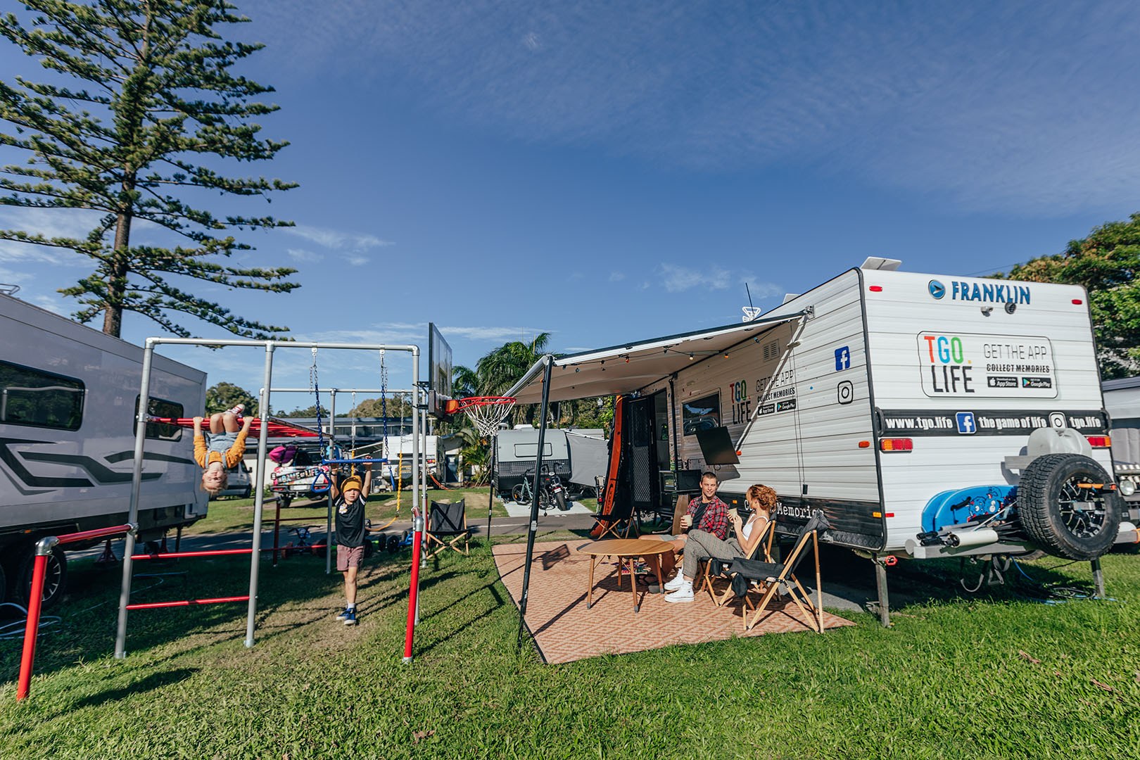 Family at their caravan site at Burleigh Beach Tourist Park. Two kids are playing on the nearby playground.