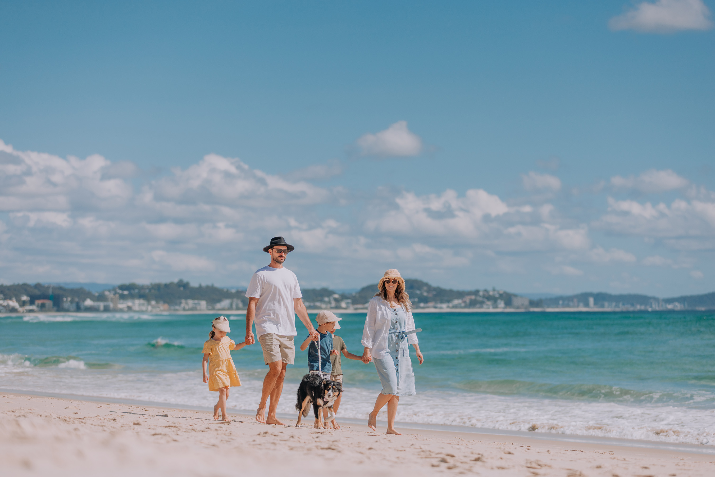 A family of four walk with their dog along Kirra Beach on a bright, sunny day.