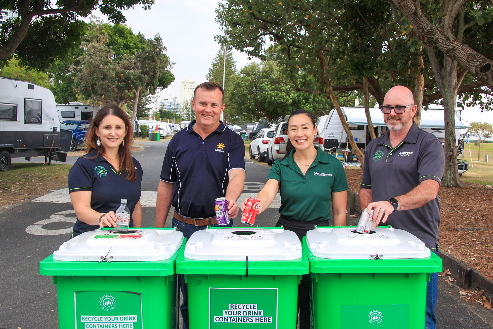 Four people standing behind a row of green recycling bins at Broadwater Tourist Park.