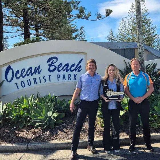 Park Managers Pete and Becky, alongside Gary Baldwin of Belgravia Leisure, posing with their Silver key award at the Ocean Beach Tourist Park entrance.