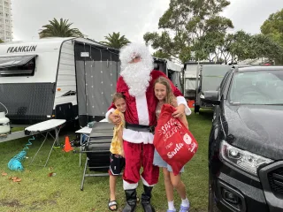 Santa standing between two park guests infront of their caravan